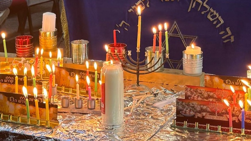 A table of glowing chanukiyot with brightly coloured candles lit