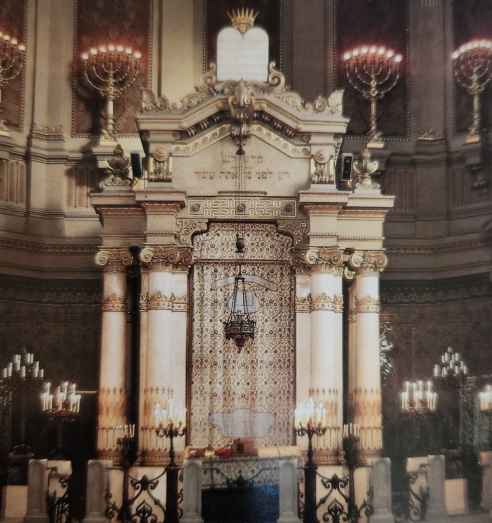 An ornate synagogue ark flanked by golden menorahs and candelabras