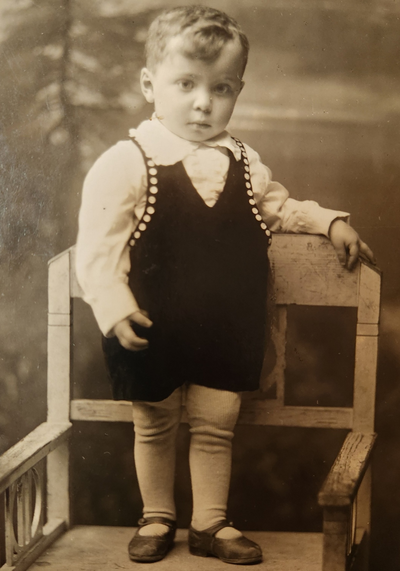 A vintage sepia portrait of a young boy standing beside a chair