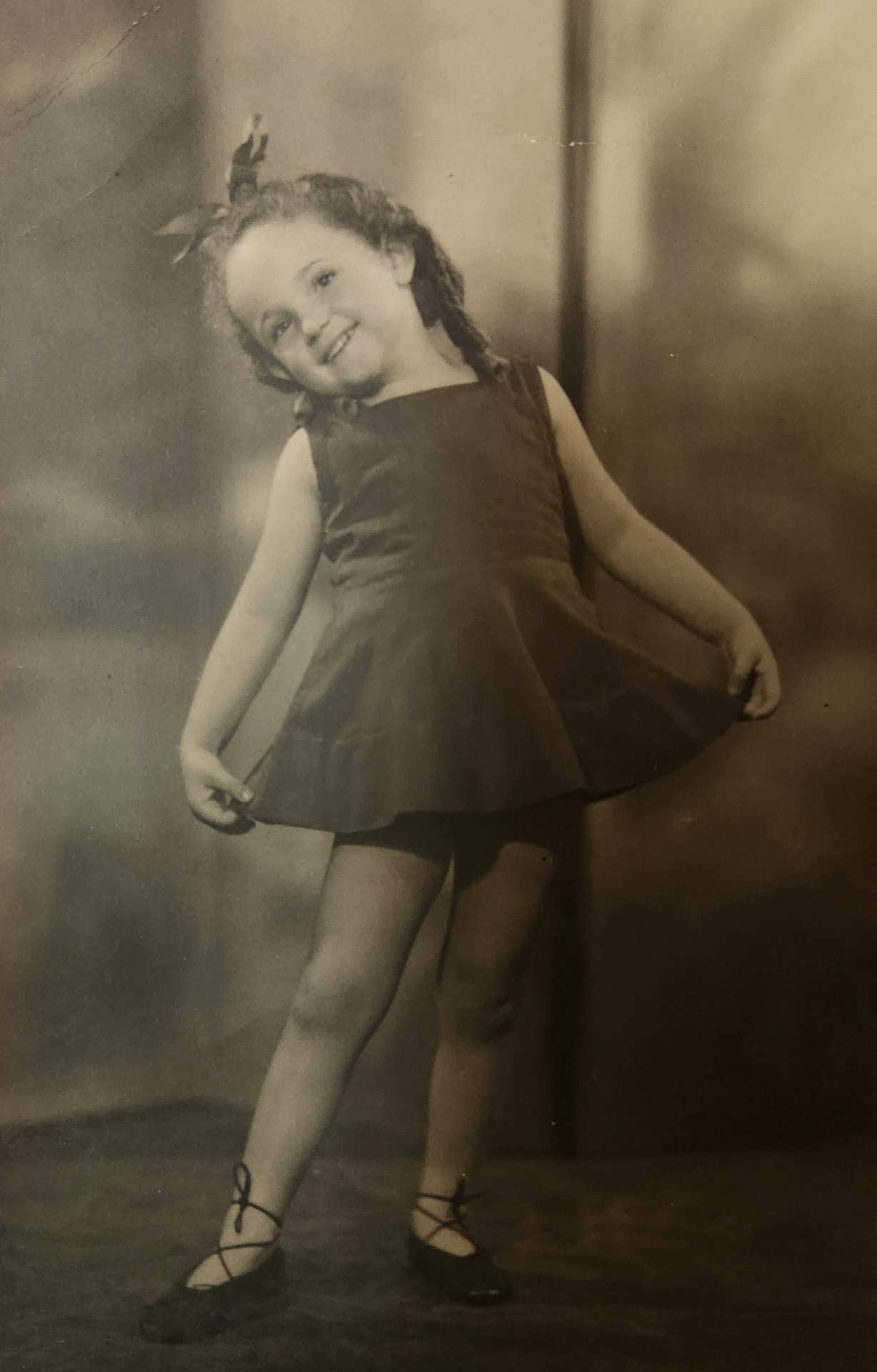 A vintage photograph of a smiling young girl posing in a dress
